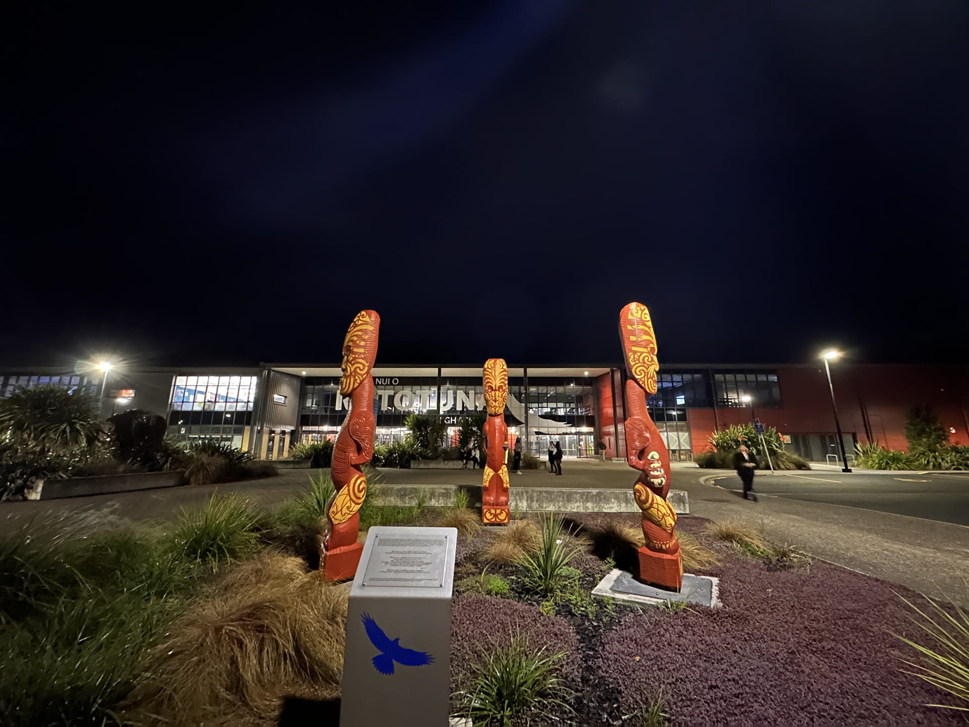 Nighttime view of the Rototuna High Schools entrance with illuminated carved pou standing at the front.