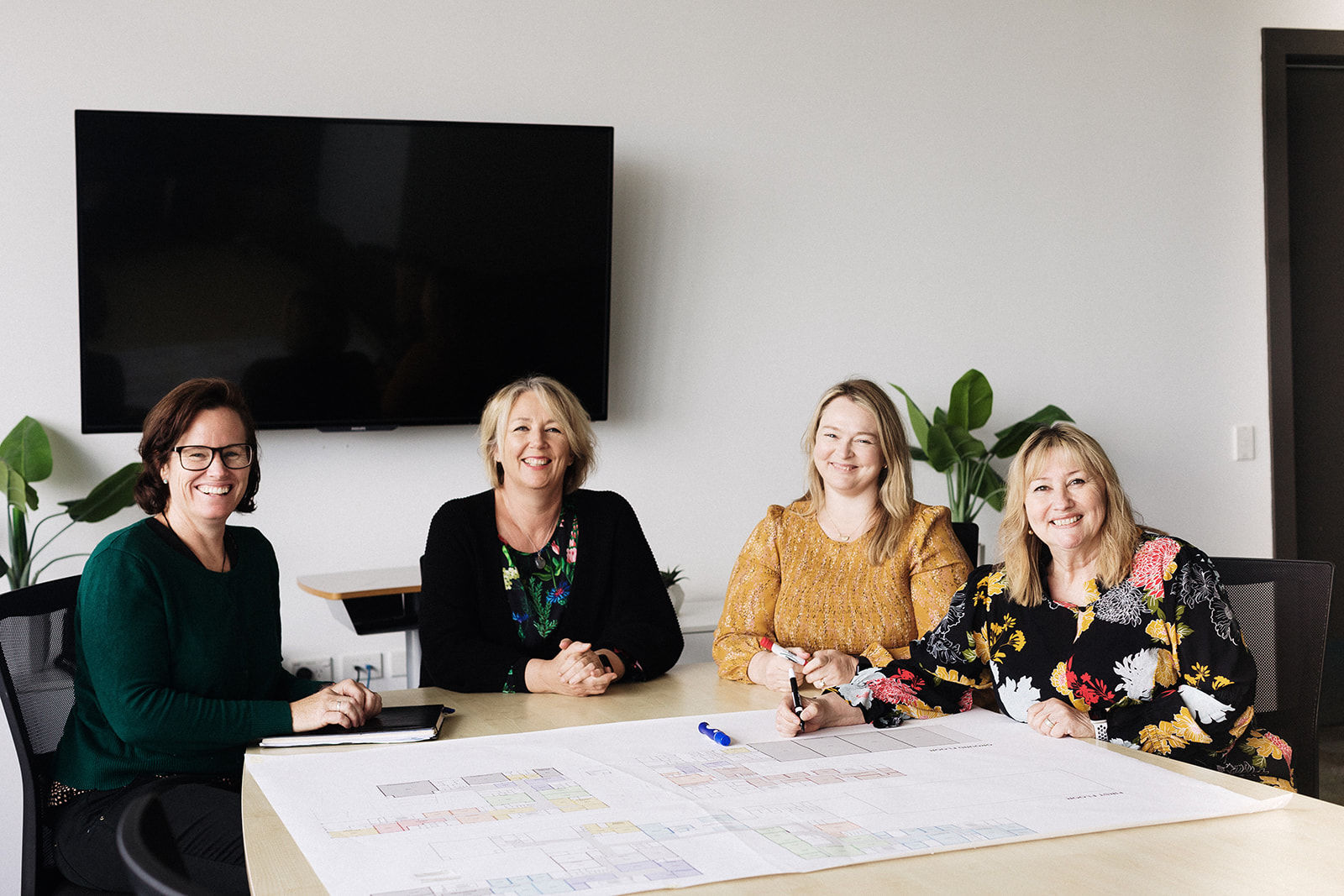 Four staff members sit around a boardroom table, smiling and relaxed, ready to discuss school plans and developments.