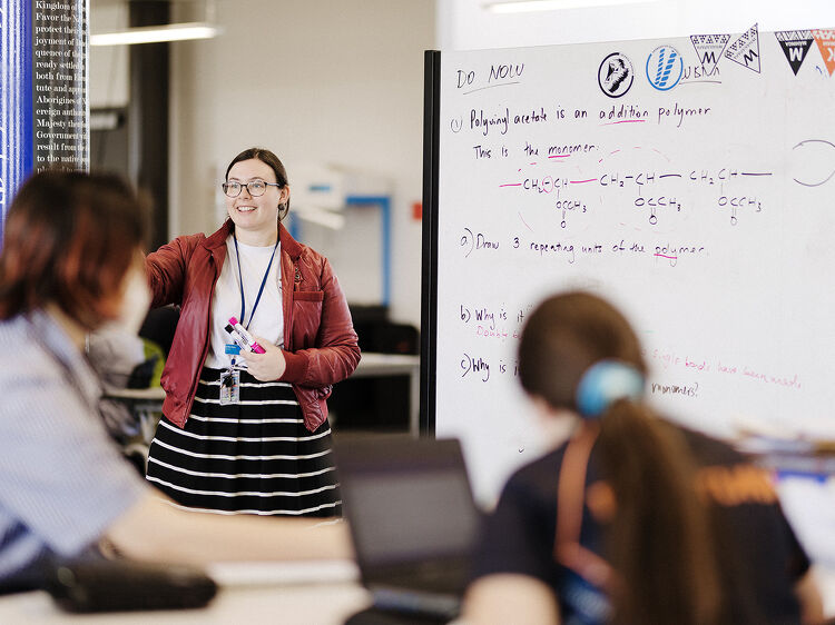 Teacher in front of a whiteboard explaining a chemistry problem to students in a classroom.