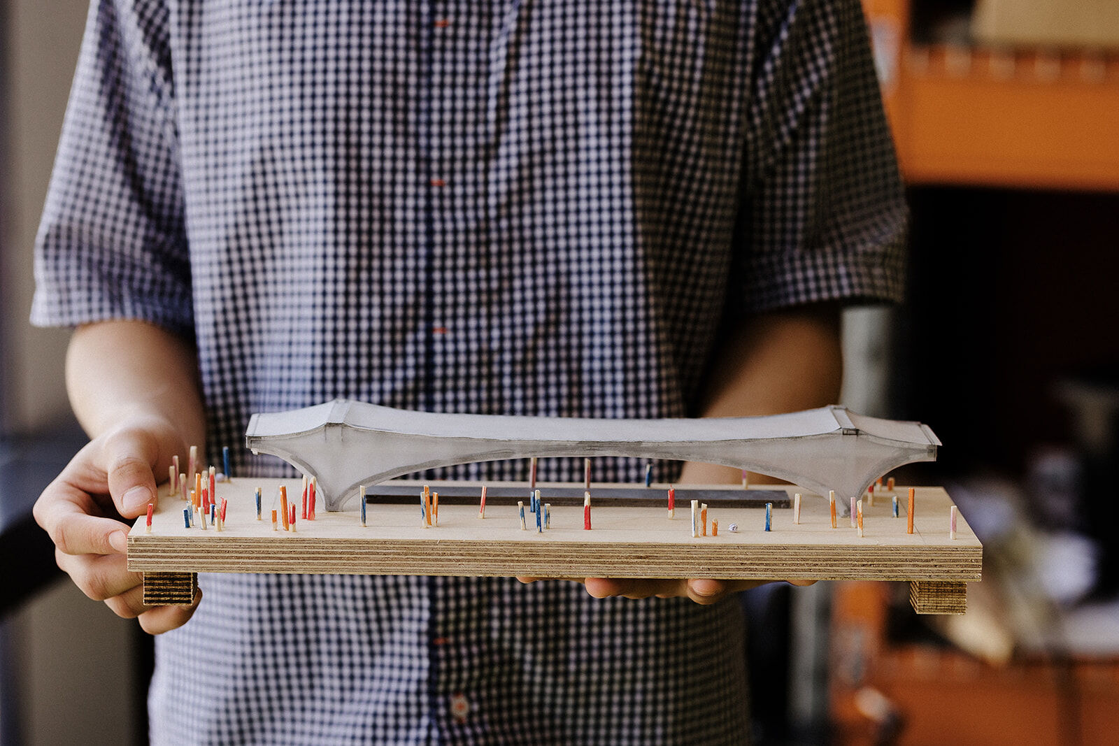Student holding a detailed architectural model of a stadium with coloured pegs.