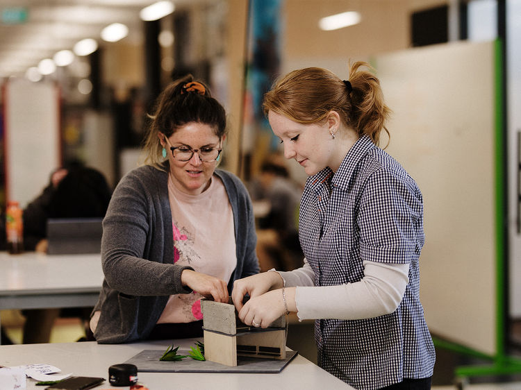 A teacher assists a student in shaping a model project in a design and tech space, both focused and collaborative.