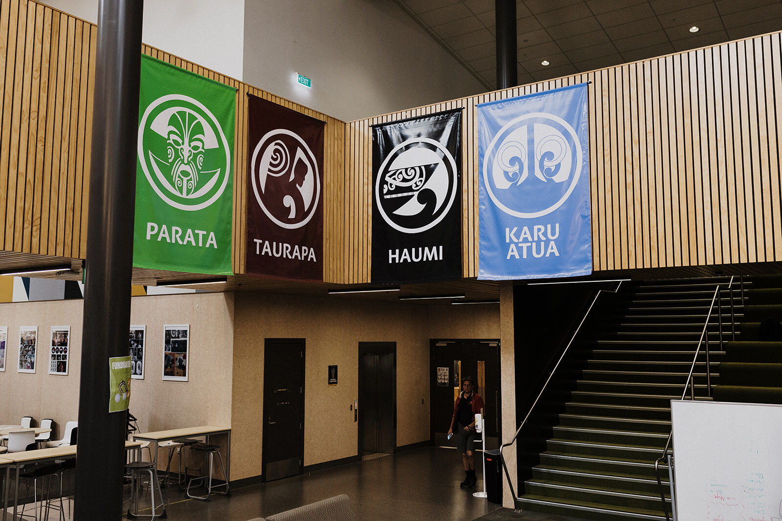 Colourful house banners—Parata, Taurapa, Haumi, Karuatua—hanging above a school hallway.