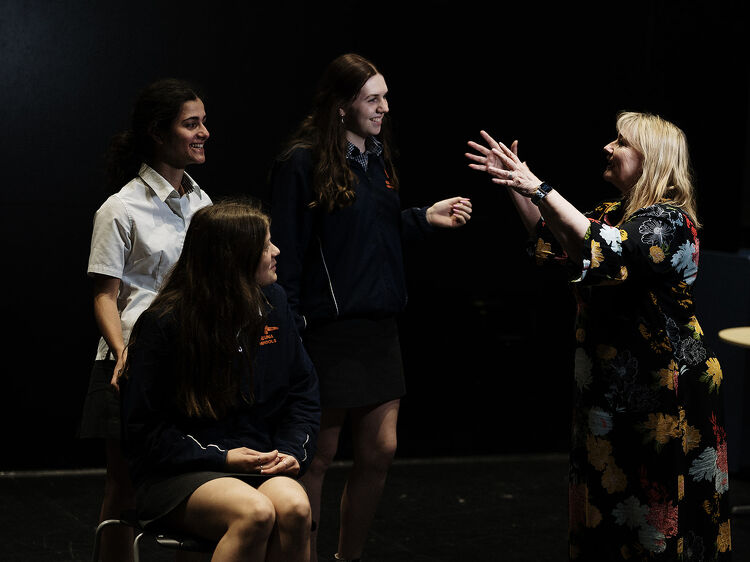 Four students on a blacked-out stage with a teacher directing them during a drama rehearsal.