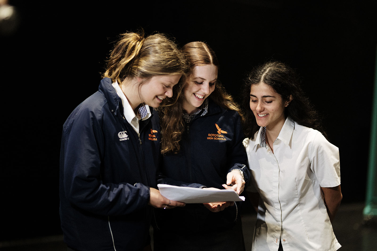 Three students smiling and reading a script together in a drama class setting