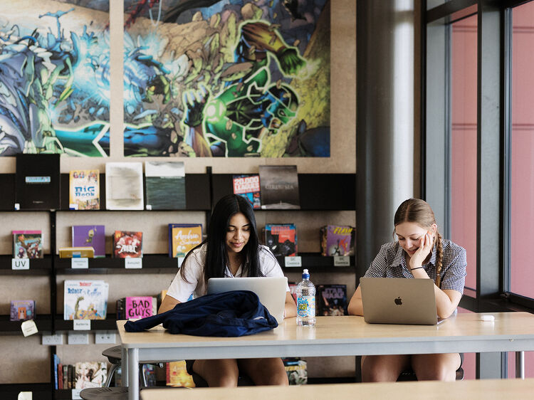 Two girls sitting at a desk together with laptops studying