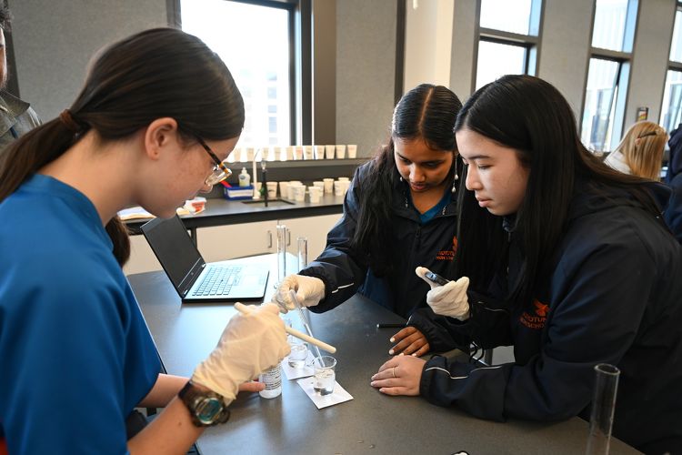 Three students in science lab uniforms conducting a pipette experiment together at Rototuna High School.