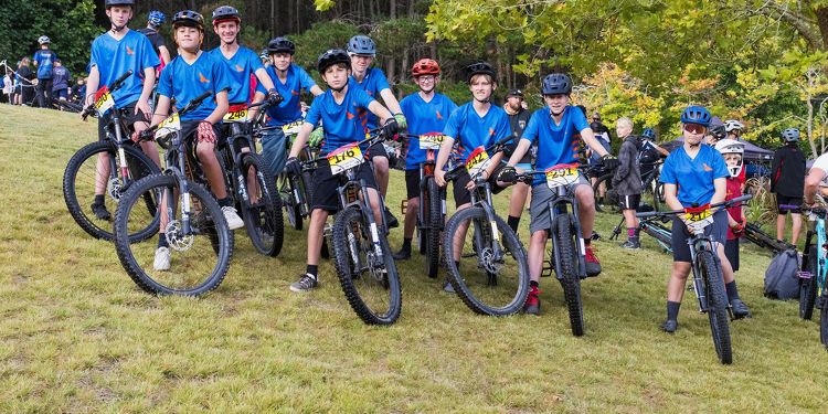 Group of Rototuna High School students in blue sports uniforms lined up with mountain bikes on a grassy hill before a race.