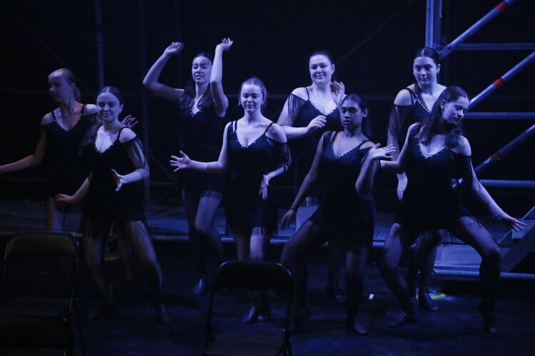 Group of students dressed in black costumes performing a choreographed dance on stage.
