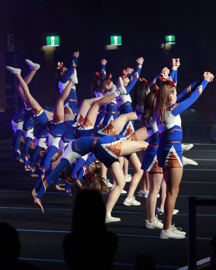 Cheerleading team mid-routine performing flips and stunts under stage lights