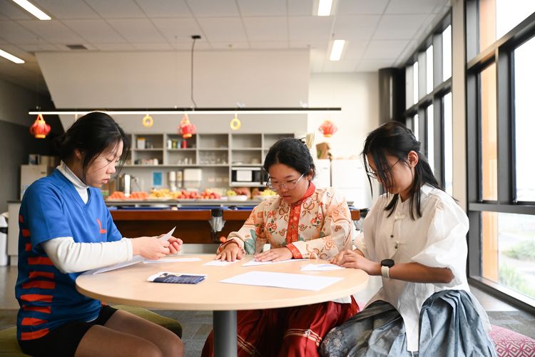 Three students in cultural attire working at a round table in a decorated common room at Rototuna High School.