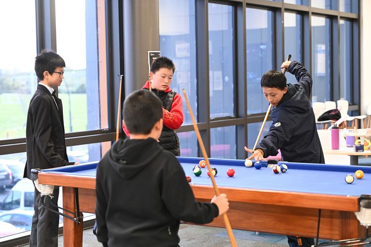 Group of students gathered around a pool table, playing a game inside a common area at Rototuna High School.