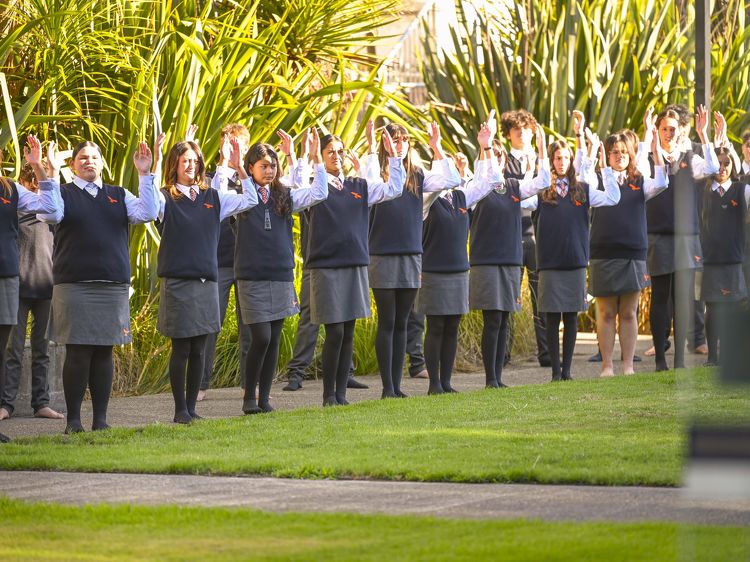 Students standing in formation with arms raised during a school pōwhiri outside