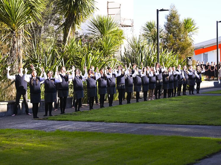 Large student group performing a haka or cultural waiata outside, lined up in uniform against greenery.
