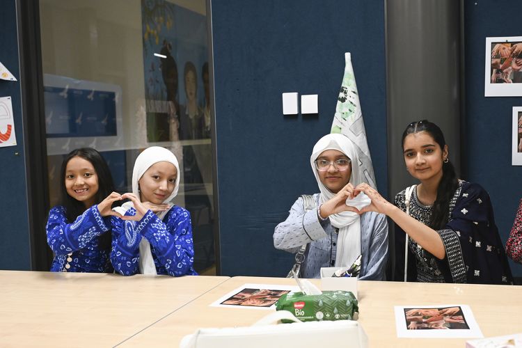 Four students sitting at a table making heart shapes with their hands, wearing cultural clothing.