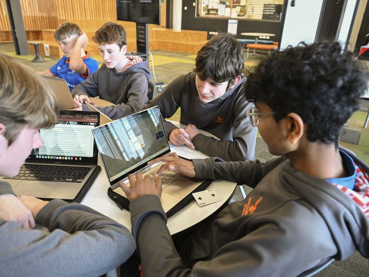 Group of students in grey Rototuna High School hoodies working collaboratively on laptops at a round table.