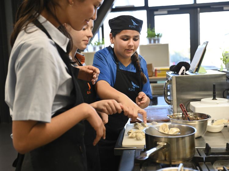 Students in RJHS-branded aprons preparing food together during a cooking class at Rototuna Junior High School.