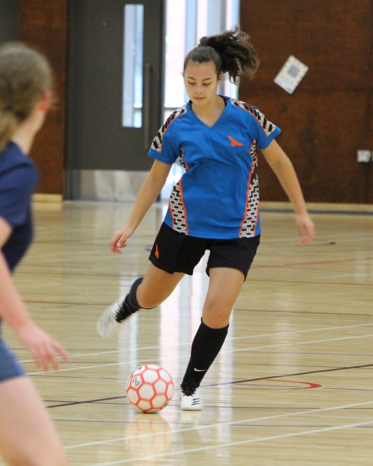 Female futsal player dribbling a red-and-white ball on indoor court