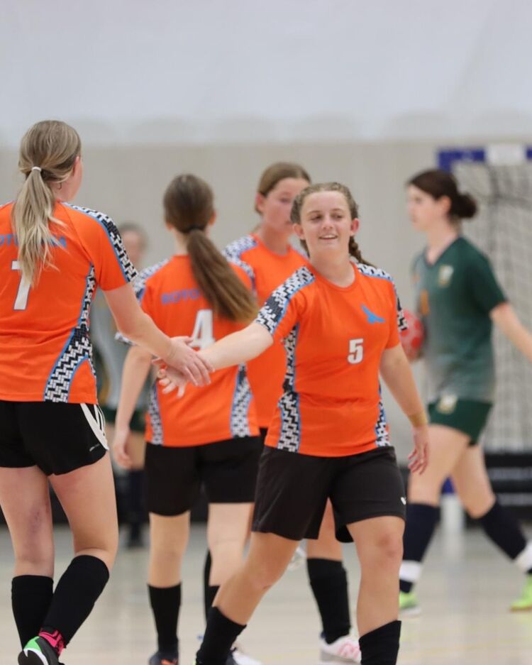 Girls futsal players in orange kits giving high-fives after a match