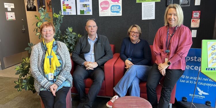Four staff members sitting and smiling in the Rototuna High School counselling area with posters and signage behind them.