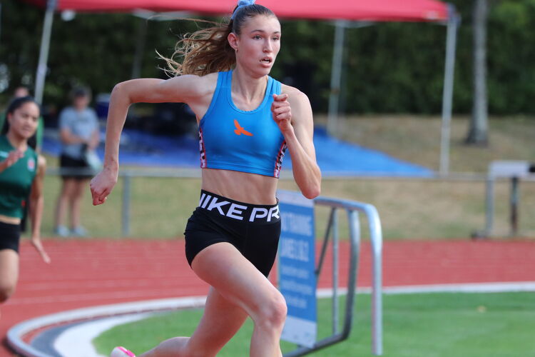 Female student sprinting on a red athletics track, focused mid-race.